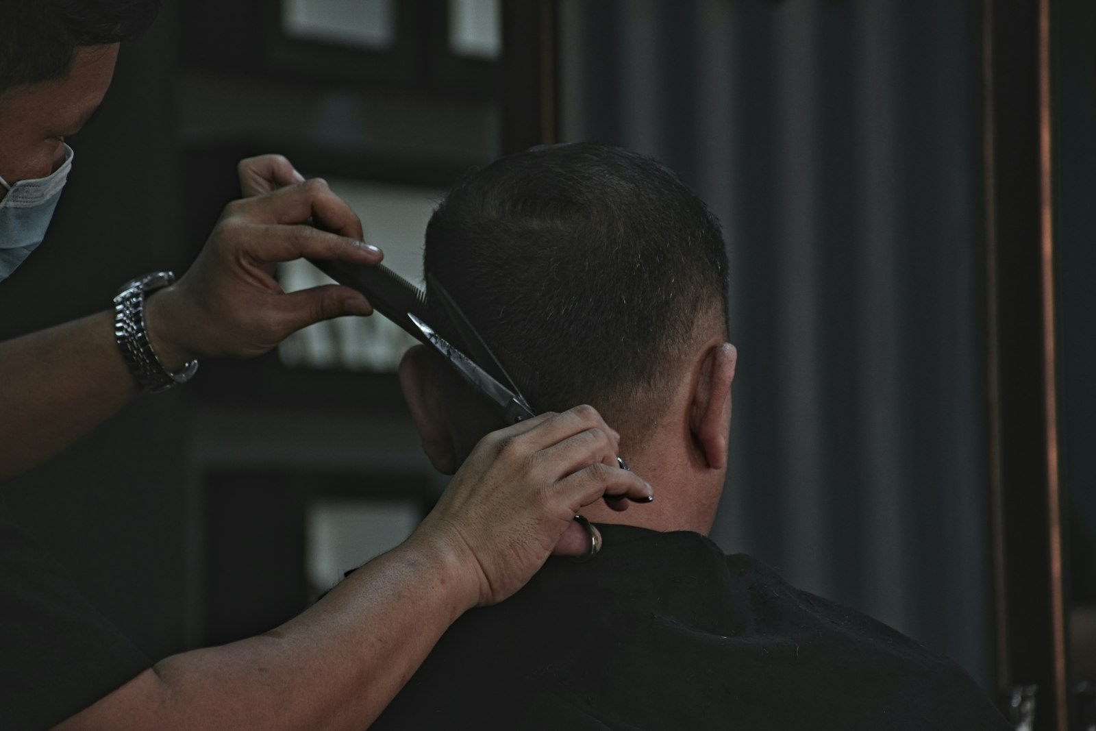 A barber trimming the back of a customer’s hair with scissors and a comb