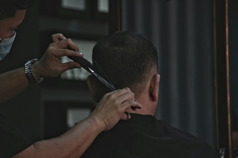 A barber trimming the back of a client’s hair with scissors