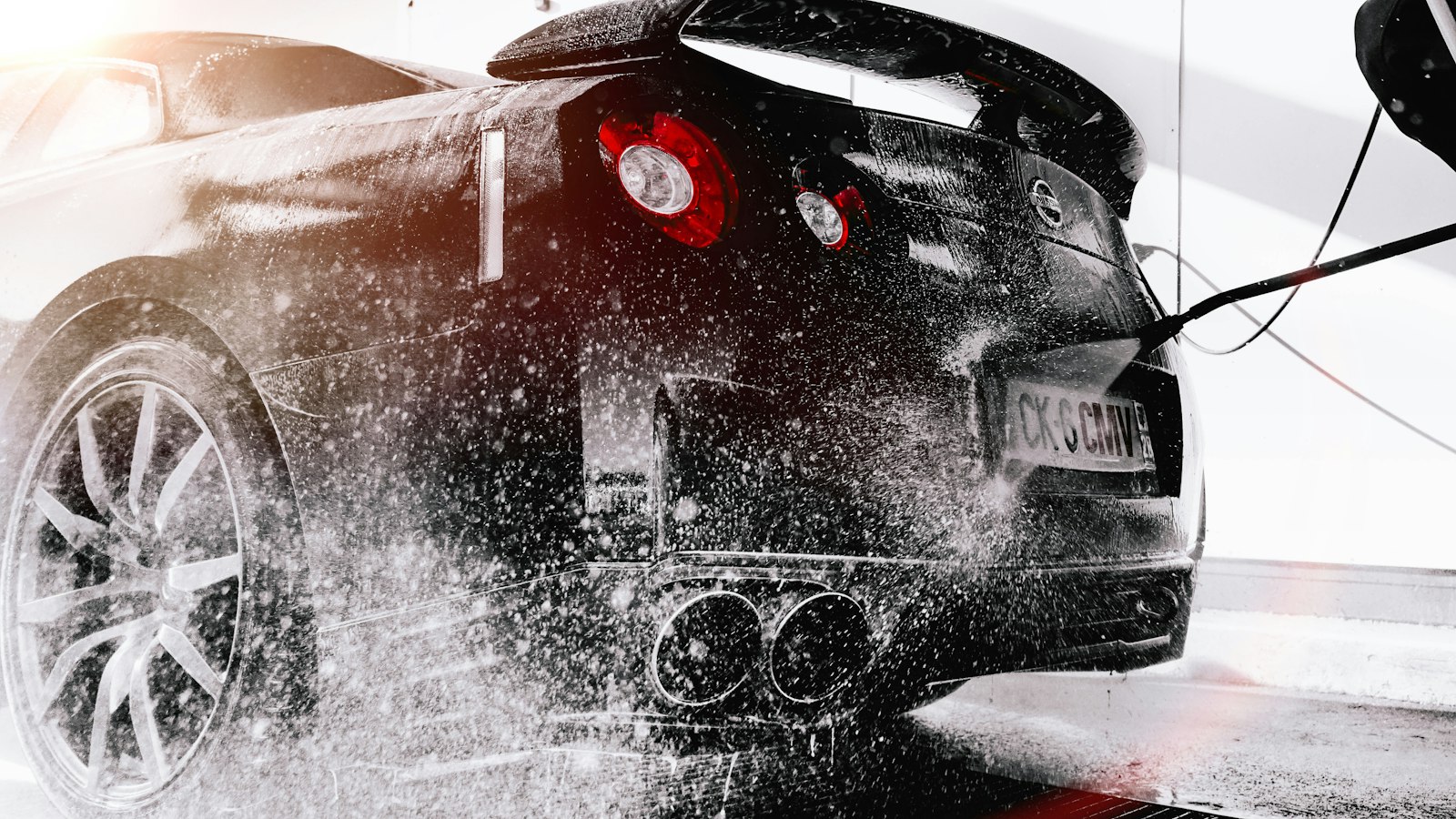 A black sports car being sprayed with water, foam flying off the rear wheel, in black and white