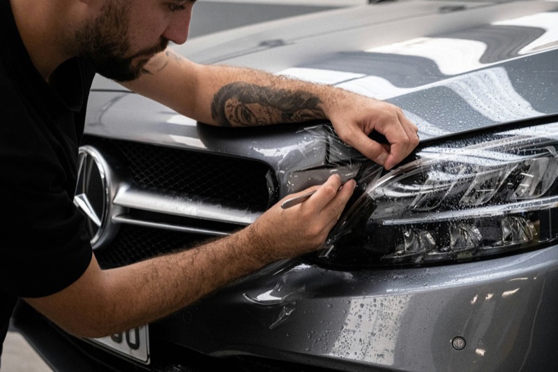 A detailer fitting protective film over the headlight of a grey car