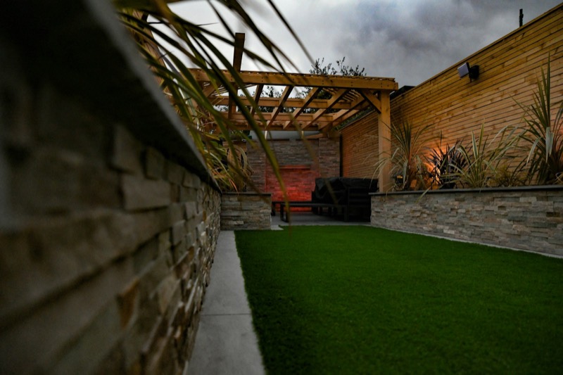 A landscaped backyard with a stone wall, pergola and lawn