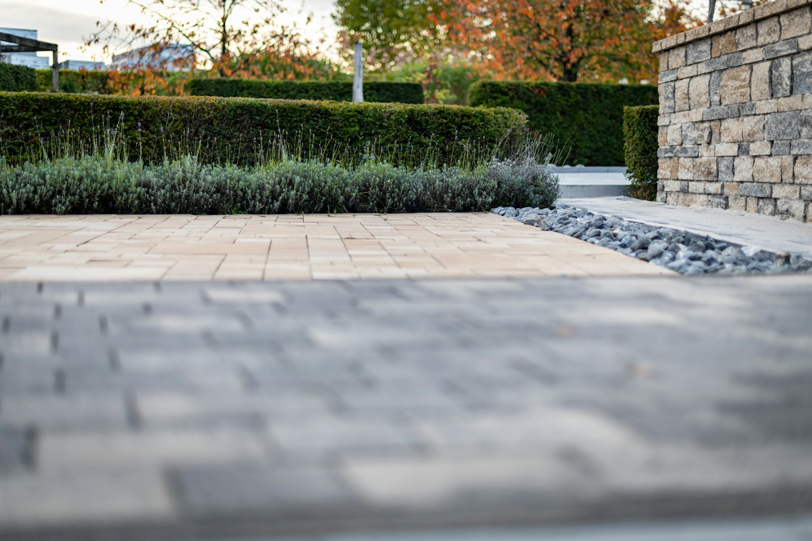 A wide paved garden path running between clipped hedges and a stacked stone wall